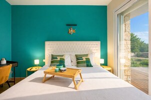 Una camera da letto con pareti color verde acqua, una testiera imbottita bianca, due comodini, un tavolino in legno con un vassoio e vista sull'esterno tramite una porta in vetro.