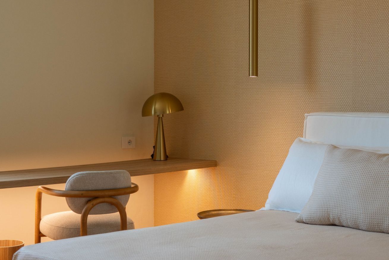 A hotel room with a bed, a chair, a lamp, and a shelf.