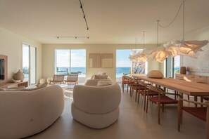 Una sala de estar moderna con un ventanal grande, un comedor con muebles de madera y vista al mar.