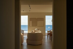 Ein modernes Interieur mit einem großen Fenster mit Meerblick, einer runden Sitzecke und einem Esstisch mit Stühlen.
