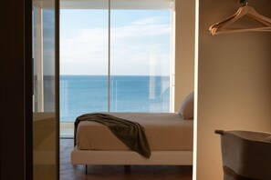 Een slaapkamer met een bed, uitzicht op zee en een schuifdeur.