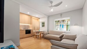 Uma sala de estar moderna com sofá, mesa de jantar com cadeiras, área de cozinha com armários e ventilador de teto.