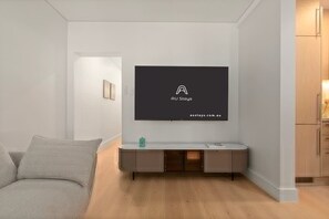 Uma sala de estar moderna com uma TV de tela plana na parede, um sofá cinza e piso de madeira.
