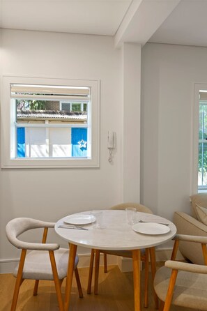 Uma área de refeições com uma mesa redonda, quatro cadeiras e uma janela com persianas.