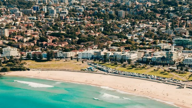 Vista aérea de uma cidade costeira, com praia, edifícios residenciais e um litoral rochoso.