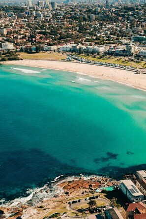 An aerial view of a coastal city with a beach, residential buildings, and a rocky shoreline. - Coastal Living 2 Bedroom in Bondi Beach (Sydney)
