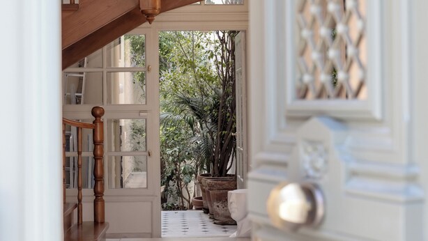 Un pasillo con escalera de madera, suelo estampado y puerta blanca con diseño de celosía.