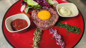 Ein Teller mit einem rohen Fleischgericht, belegt mit einem Eigelb, dazu ein gemischter Salat, Ketchup, Senf und eingelegte Zwiebeln.