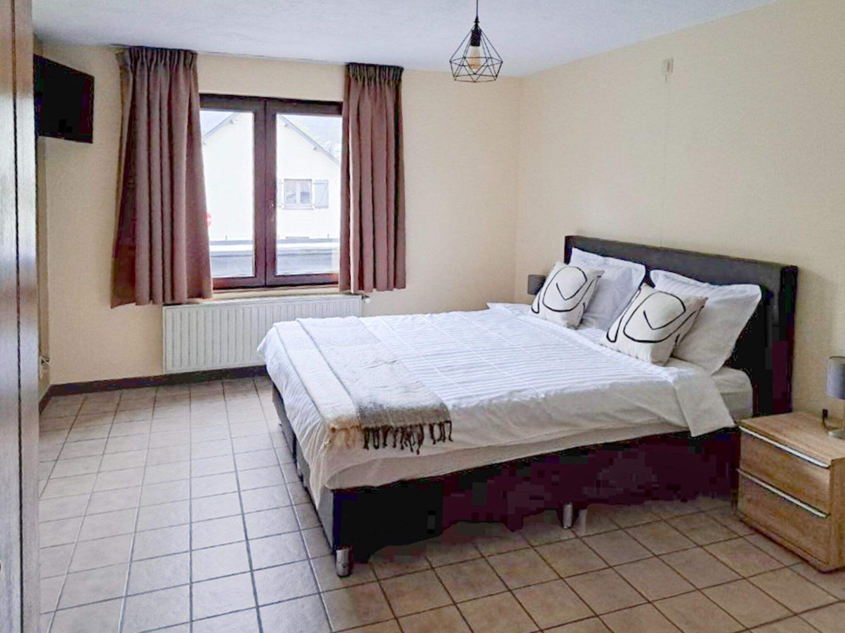Ein Schlafzimmer mit Bett, Vorhängen, Heizkörper, Fenster und Nachttisch.