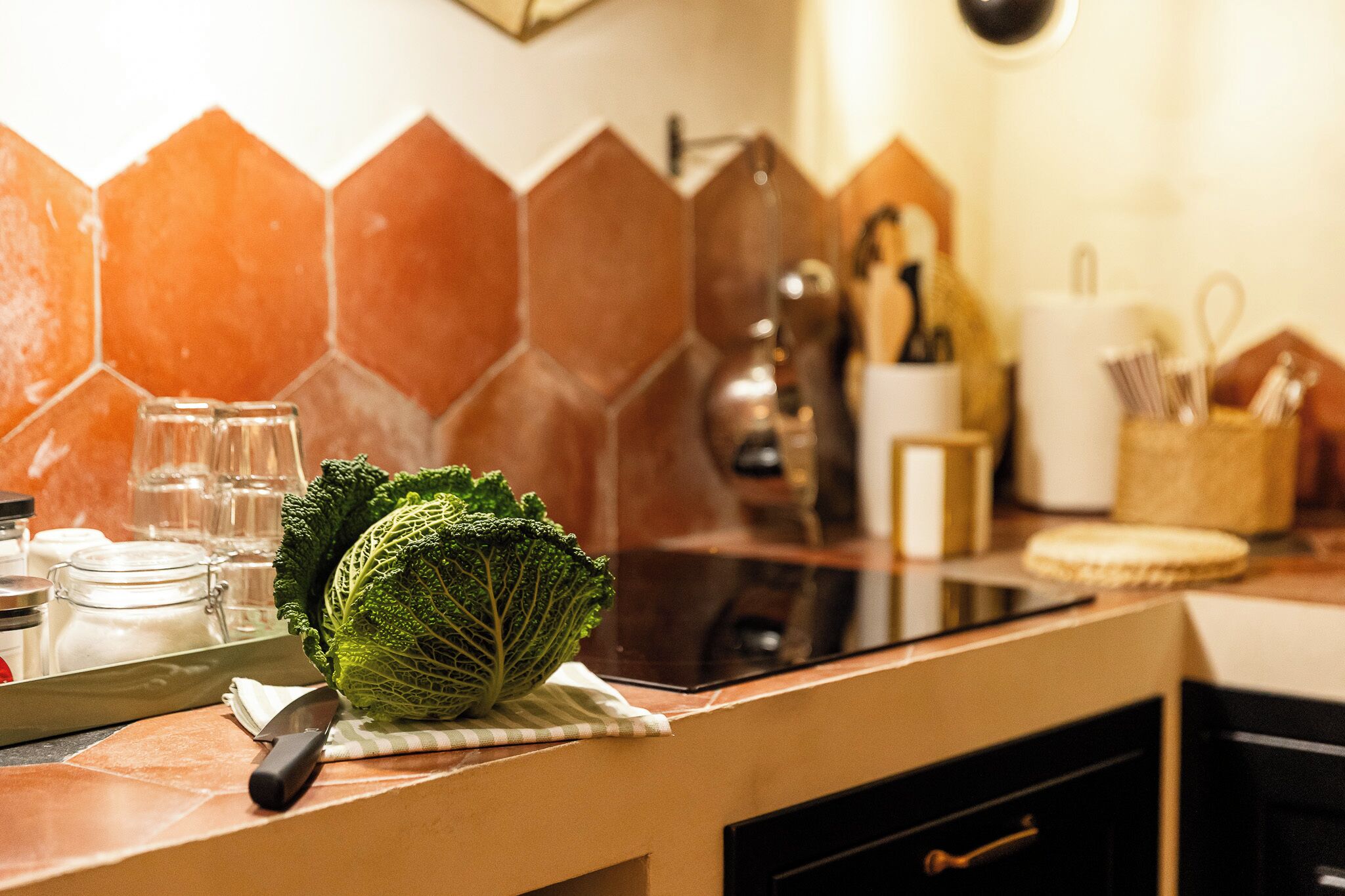 Une cuisine avec un dosseret de crédence en carreaux hexagonaux, une planche à découper avec un chou, un couteau et un bocal en verre.