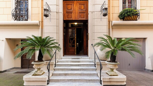 A building entrance with a set of stone steps leading to a wooden door, flanked by two potted palm trees and a wrought iron railing. - Charming apartment in Rome a stone's throw from Villa Ada and Villa Borghese (Roma)