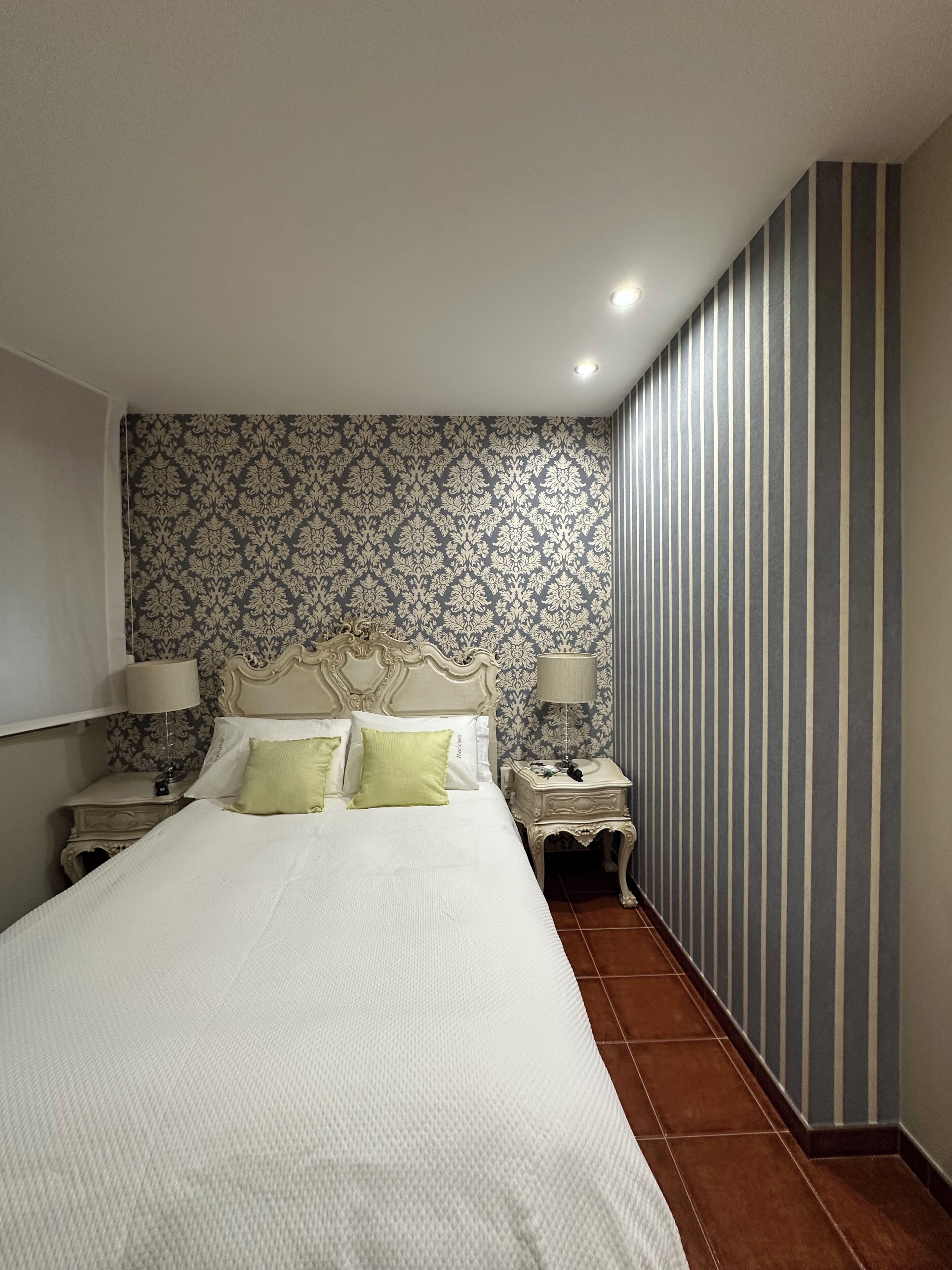 A bedroom with a large bed, two bedside tables with lamps, a patterned wallpaper, and a striped wall.