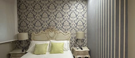 A bedroom with a large bed, two bedside tables with lamps, a patterned wallpaper, and a striped wall.