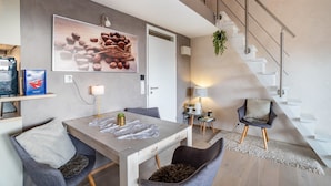 A modern living room with a dining area, a staircase, and a large wall art piece. - Apartment “Auszeitwohnung Sasbachwalden - Pool” with Shared Terrace, Balcony, Sauna & Wi-Fi (Sasbachwalden)