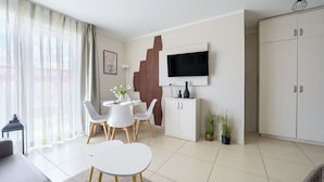 A modern living room with a dining area, a flat-screen TV mounted on the wall, and a large wardrobe. - Apartamenty Sun & Snow Baltic Cliff (Niechorze)