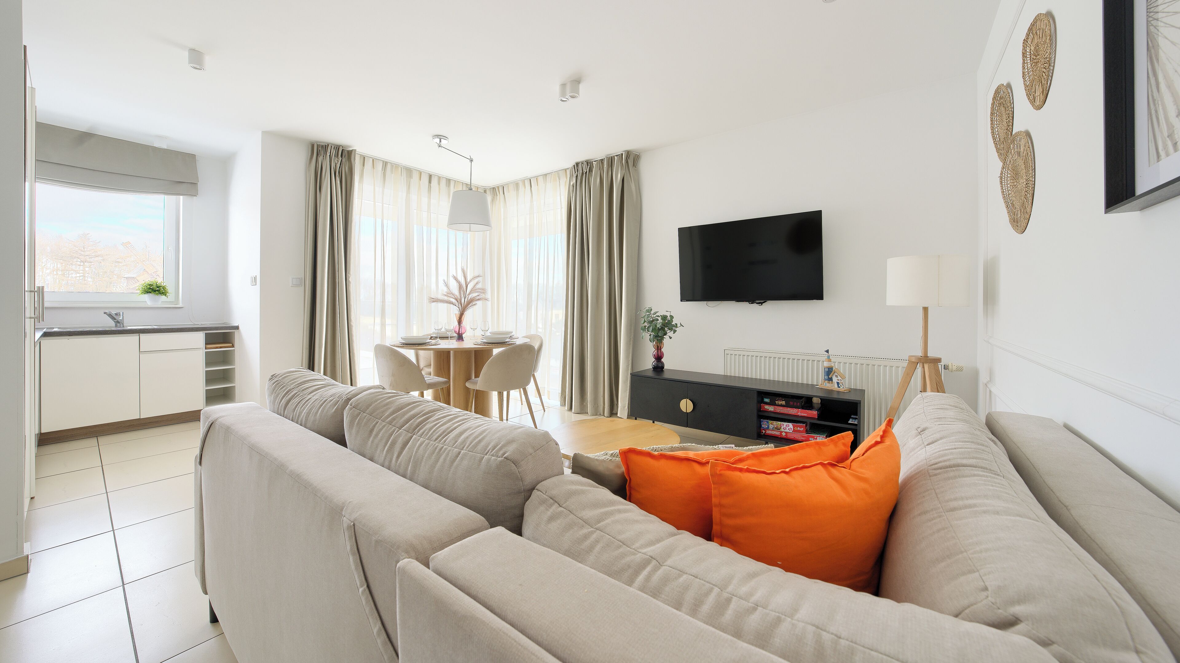 Een moderne woonkamer met een bank, een eethoek en een aan de muur bevestigde televisie.