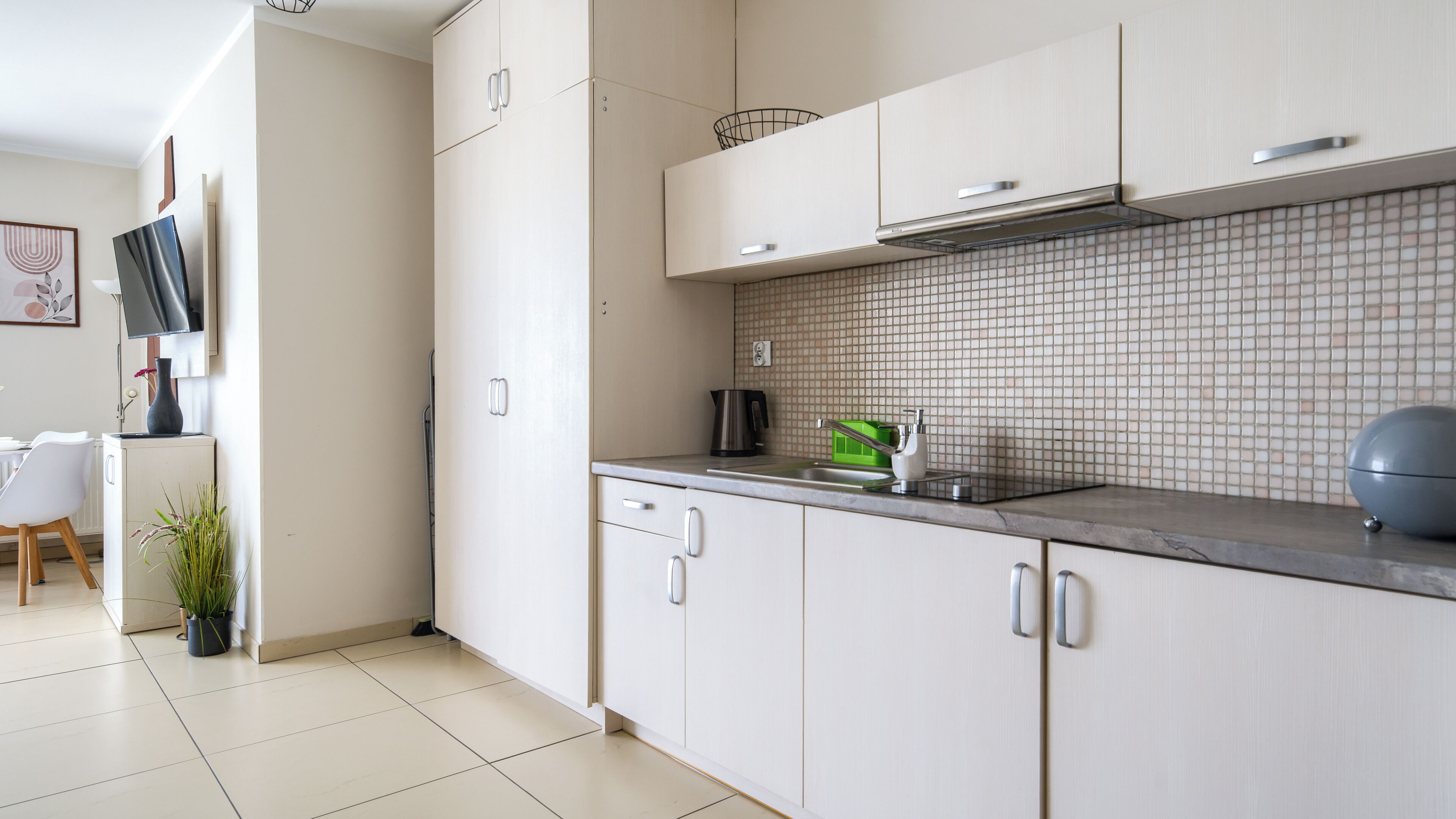A modern kitchen with white cabinets, a tiled backsplash, and a flat-screen TV mounted above the counter.