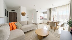 A modern living room with a sofa, a round wooden coffee table, and a dining area with a table and chairs. - Apartamenty Sun & Snow Baltic Cliff (Niechorze)