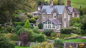 A large stone house with multiple windows and a conservatory, surrounded by lush gardens and a well-maintained lawn. - The Old Rectory - 5 Bedroom Holiday Home - Llanedi (Swansea)