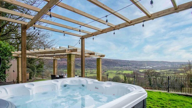 A hot tub under a wooden pergola with a scenic view of hills and fields. - The Old Rectory - 5 Bedroom Holiday Home - Llanedi (Swansea)