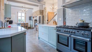 A modern kitchen with a large island, double ovens, and a stone fireplace. - The Old Rectory - 5 Bedroom Holiday Home - Llanedi (Swansea)