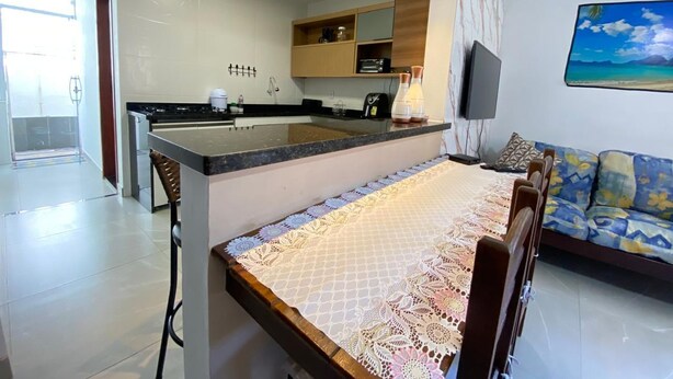 A modern kitchen with a central island, a dining area with a table and chairs, and a living room with a sofa and a TV. - Teresa's House - Beach and Comfort (Cabo Frio)