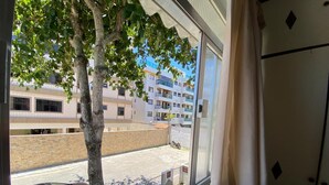A window view of a parking lot with a tree, a building with multiple floors, and a car. - Teresa's House - Beach and Comfort (Cabo Frio)