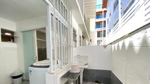 A compact, industrial-style bathroom with a washing machine, a sink, and a trash bin. - Teresa's House - Beach and Comfort (Cabo Frio)