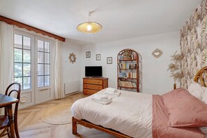 Ein Schlafzimmer mit Bett, Fernseher, Bücherregal und Essecke mit Stühlen.