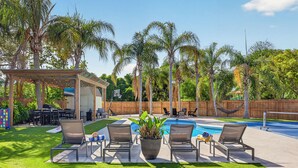 A backyard with a pool, lounge chairs, a pergola, and palm trees. - 2 homes • 2 Pools • 2 Courts • Sleeps 18 (Jacksonville Beach)