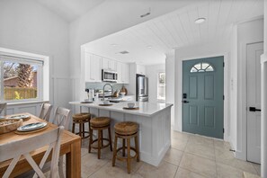 A modern kitchen with white cabinetry, a central island with stools, and a teal door. - 2 homes • 2 Pools • 2 Courts • Sleeps 18 (Jacksonville Beach)
