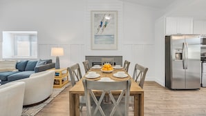 A dining area with a wooden table set for six, surrounded by grey chairs. A modern kitchen with a stainless steel refrigerator is visible to the right. - 2 homes • 2 Pools • 2 Courts • Sleeps 18 (Jacksonville Beach)