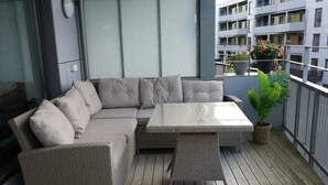 A balcony with a wicker sofa, a glass-top table, and potted plants. - Apartment in a quiet area at Lade (Trøndelag)