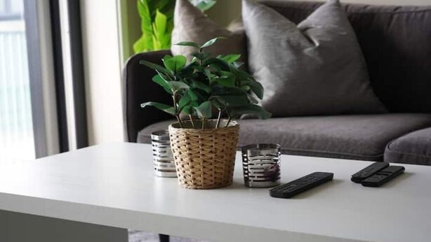 A white table with a woven plant pot, two remote controls, and a stack of books. - Apartment in a quiet area at Lade (Trøndelag)