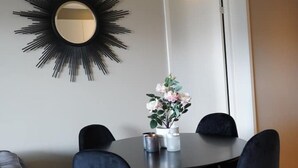 A dining area with a round table, black chairs, a vase with flowers, and a black sunburst mirror on the wall. - Apartment in a quiet area at Lade (Trøndelag)