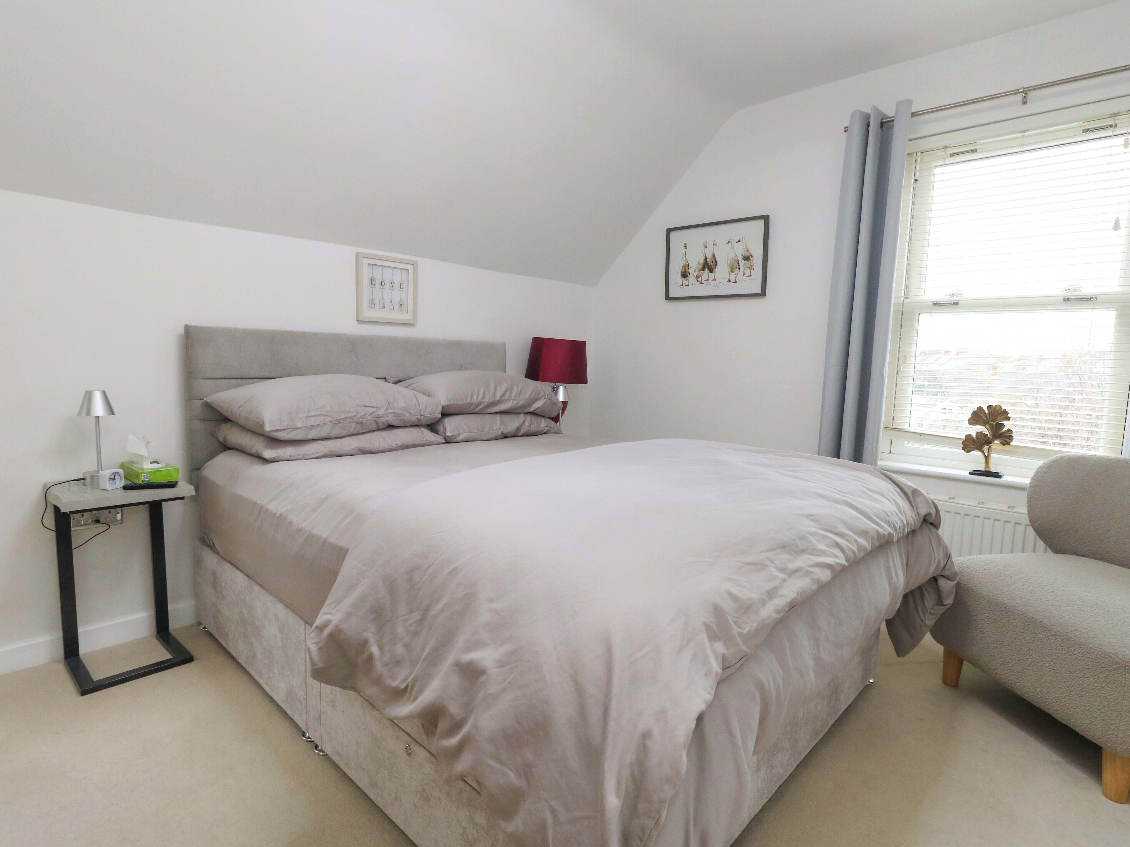 A bedroom with a bed, bedside table, lamp, and a window with curtains.