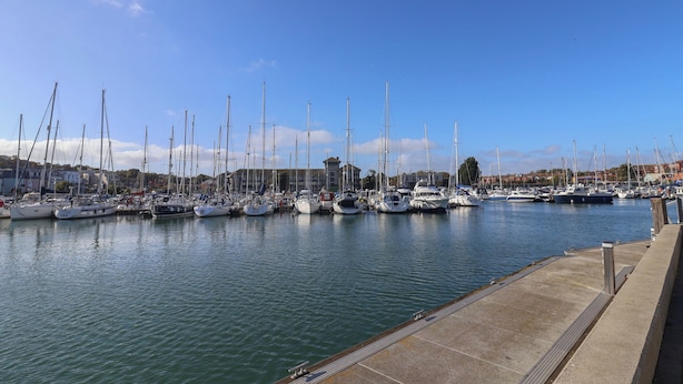 A marina with multiple sailboats docked along a waterfront promenade. - Harbour Reach 7 (Weymouth)