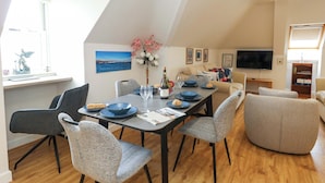 A dining area with a table set for four, surrounded by chairs, a TV, and a bookshelf. - Harbour Reach 7 (Weymouth)
