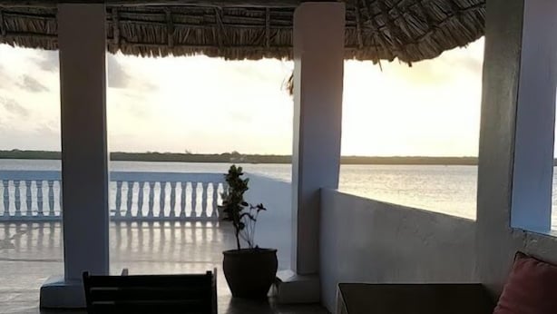A covered outdoor seating area with a bench and a sofa, overlooking a body of water. - Stopover Guest House Lamu Town (Lamu)