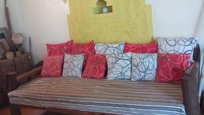 A room with a sofa bed, a decorative wall piece, and a small shelf with a vase. - Stopover Guest House Lamu Town (Lamu)