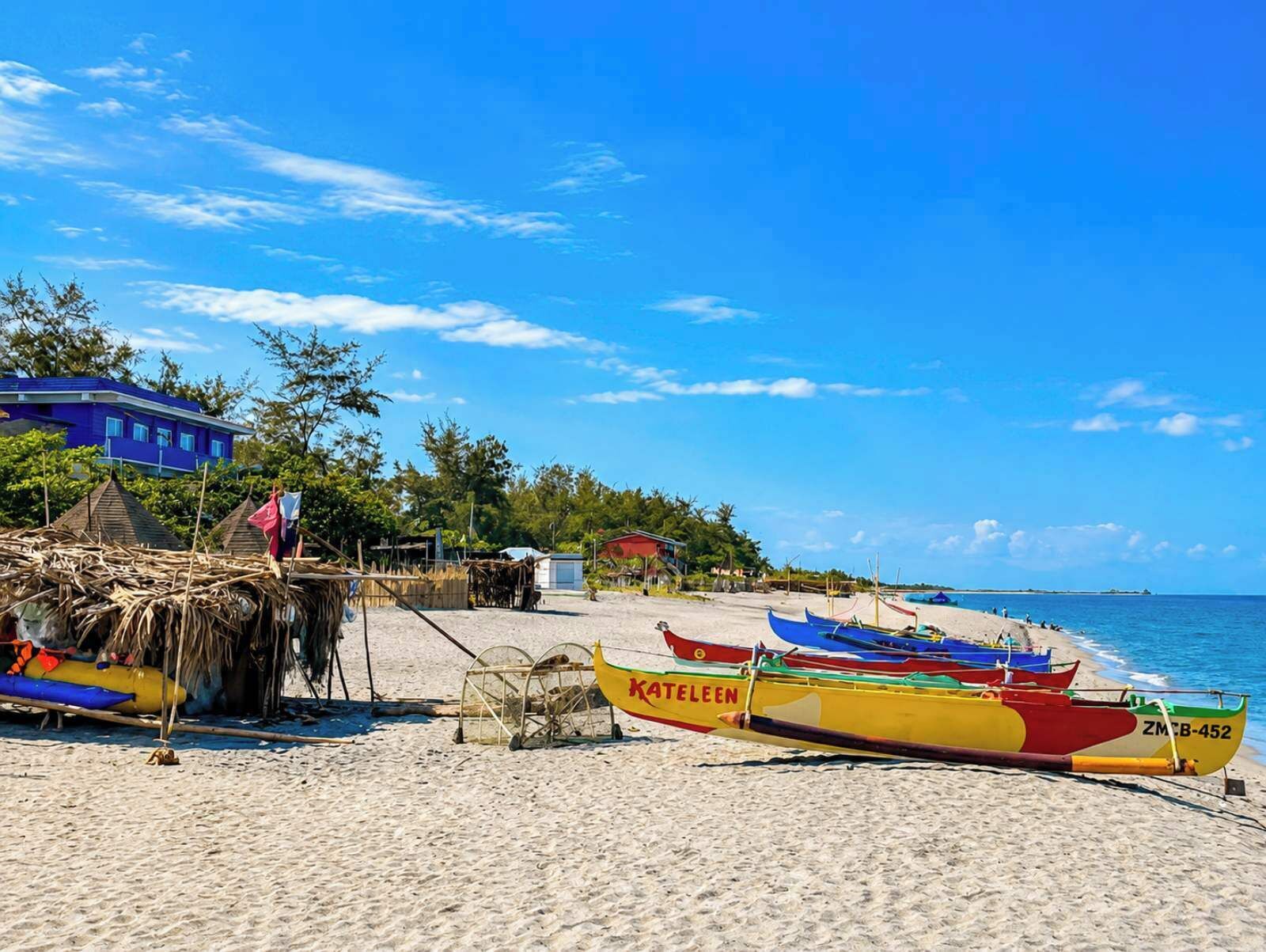 A beach with colorful boats, a blue building, and a thatched structure.
