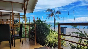 Un balcone con vista sulla spiaggia, dotato di ringhiera in legno, una sedia e piante in vaso.