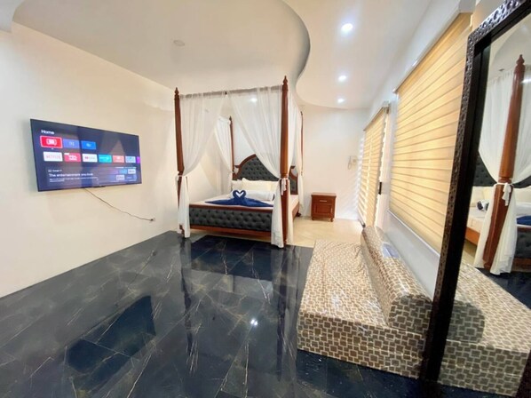 A modern bedroom with a four-poster bed, a flat-screen TV mounted on the wall, and a tiled floor. - Eden Beach Resort Zambales (Cabangan)