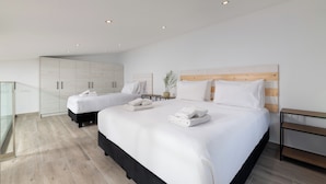 Ett modernt hotellrum med två sängar, en sänggavel i trä, ett litet bord och en glasvägg.