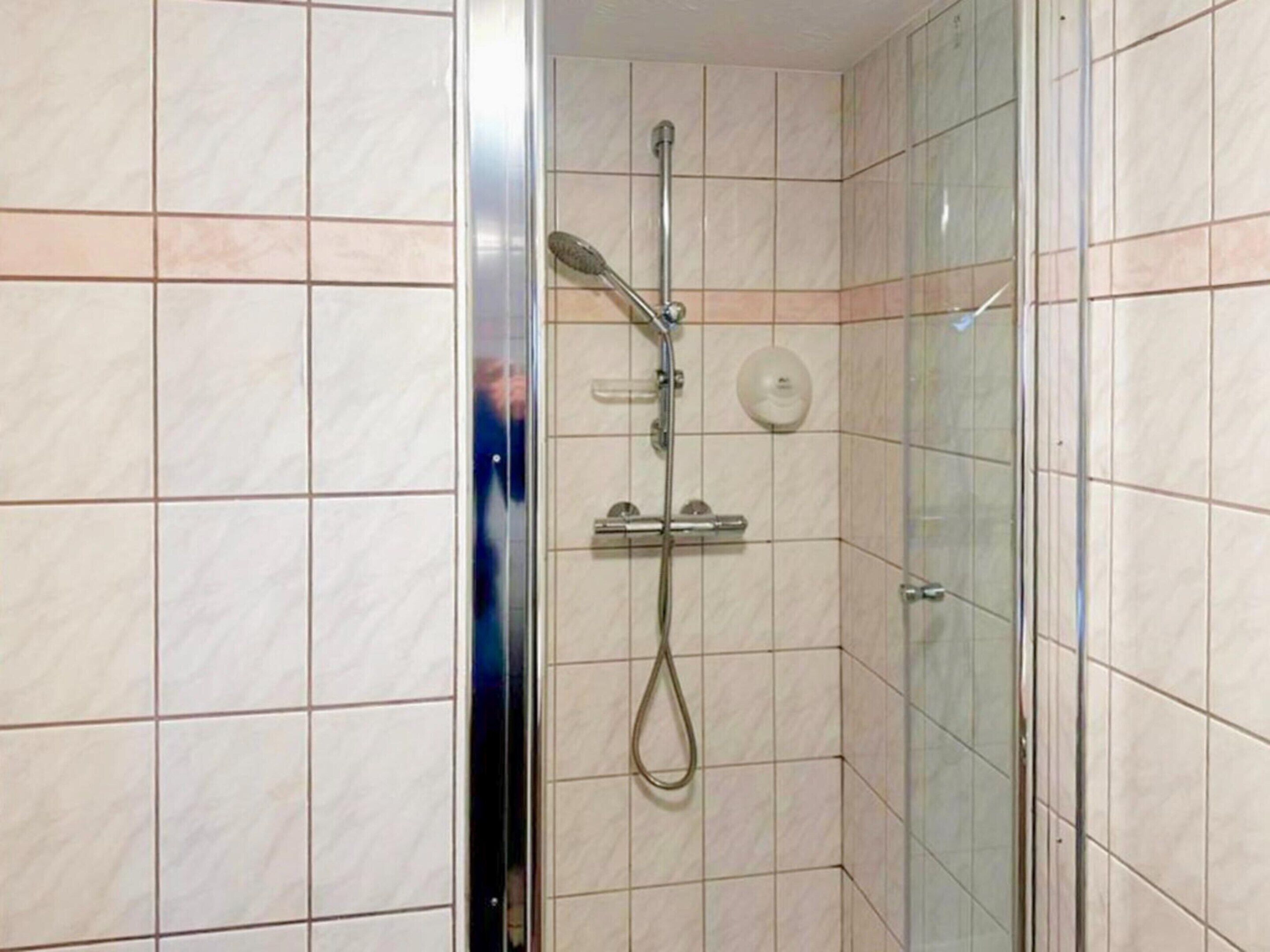 A glass-enclosed shower with a handheld showerhead and a wall-mounted control panel.