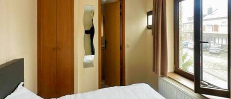 Habitación de hotel con cama, armario de madera, espejo, ventana con cortinas y radiador.