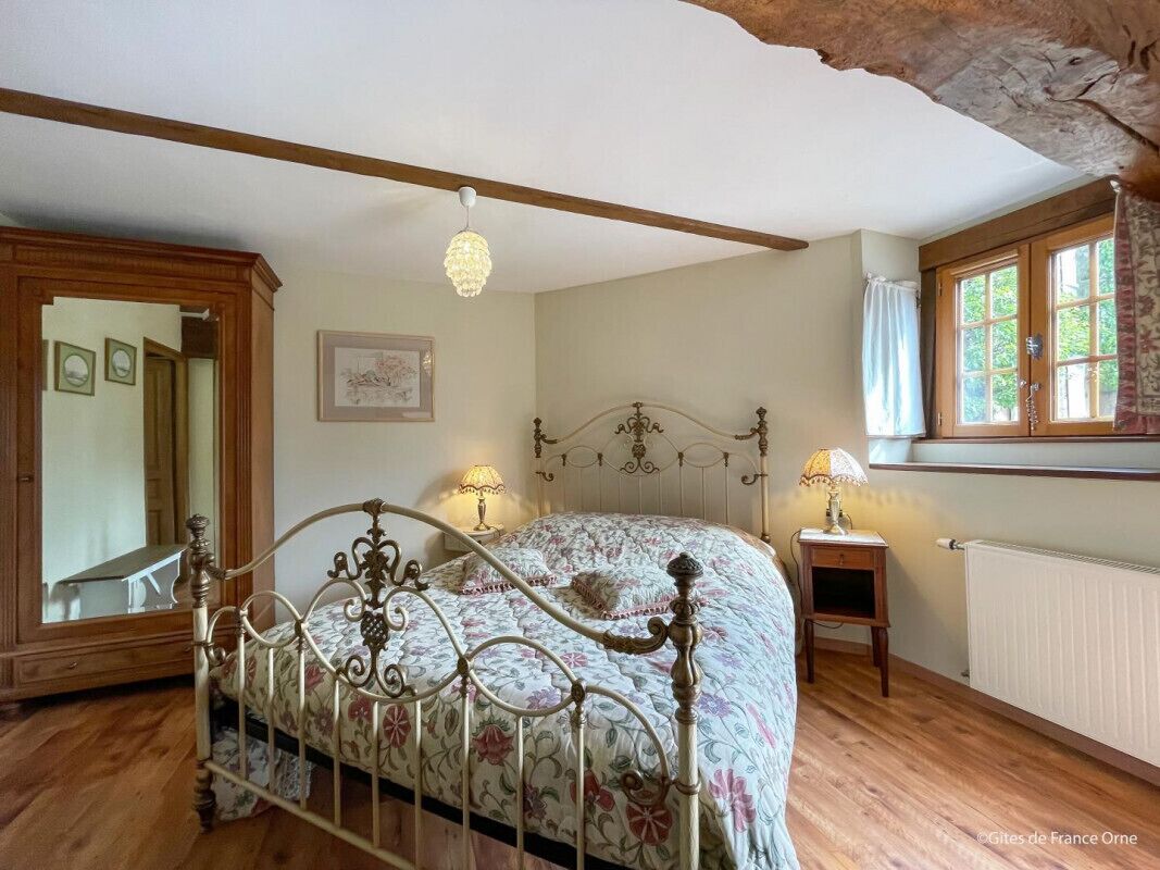 A bedroom with a bed, wooden floor, a window with curtains, a radiator, and a mirror.