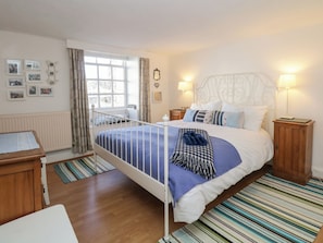A bedroom with a bed, bedside tables, a window with curtains, a radiator, and wall decorations.