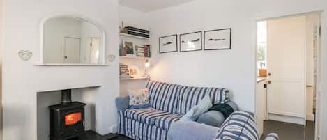 A cozy living room with a sofa, a fireplace, a bookshelf, and a door leading to another room.