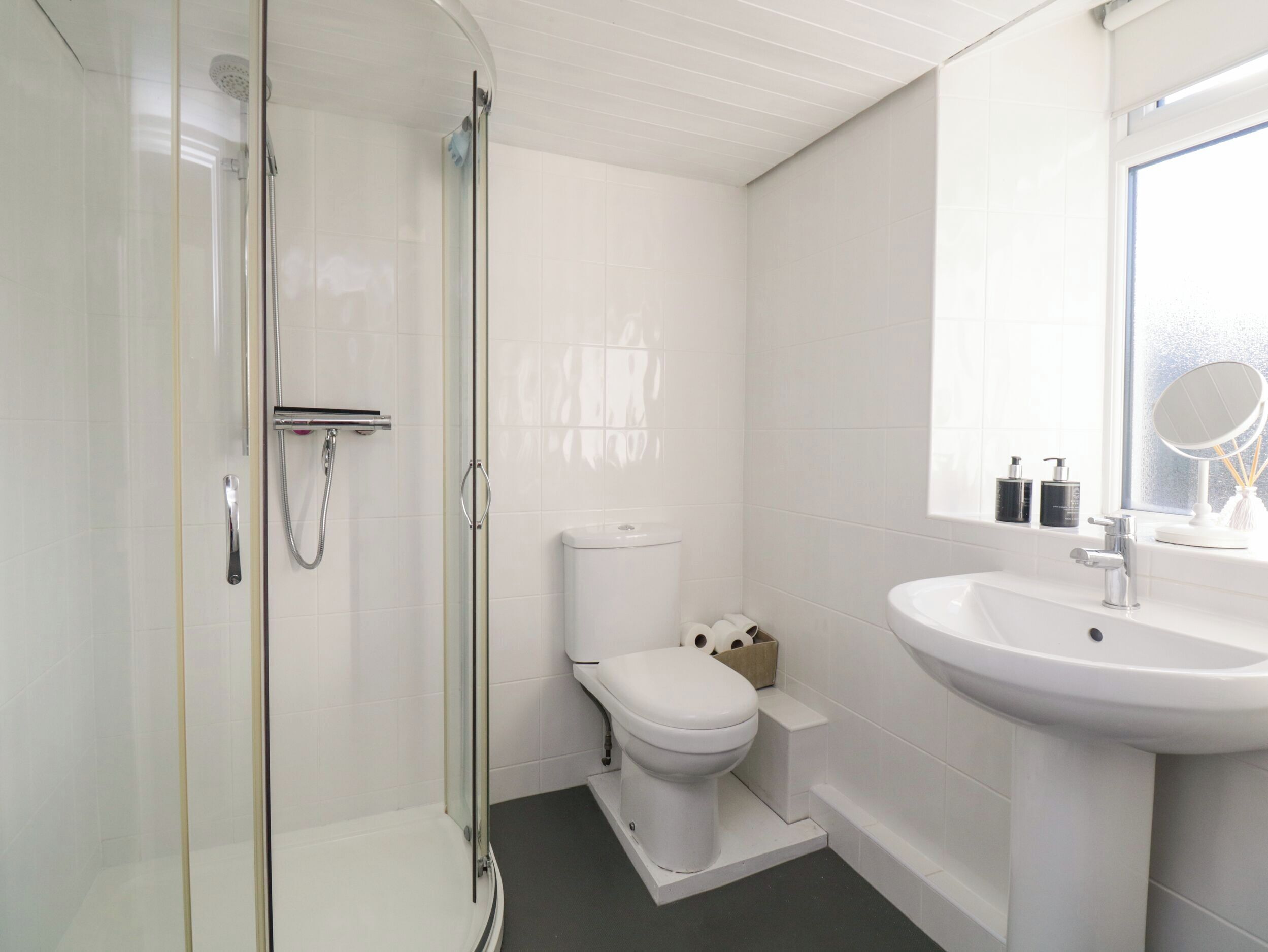 A modern bathroom with a glass-enclosed shower, a white toilet, and a sink with a mirror above it.